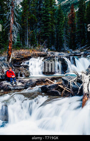 Frau sitzt neben einem Wasserfall. Stockfoto