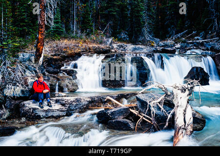 Frau sitzt neben einem Wasserfall. Stockfoto