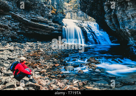 Frau sitzt neben einem Wasserfall. Stockfoto