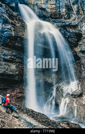 Frau sitzt neben einem Wasserfall. Stockfoto