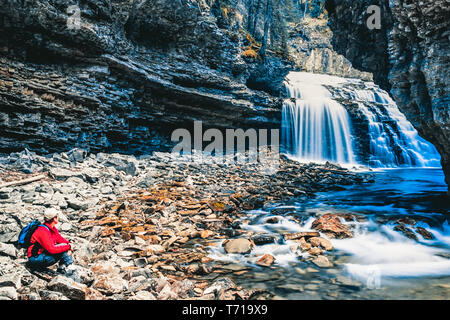 Frau sitzt neben Wasserfall am Johnston Canyon. Banff Nationalpark, Kanada. Stockfoto