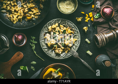 Mit vegetarische Tortellini Pasta mit Gemüse, Kräutern und Pilzen auf dunklen rustikalen Küche Tisch Hintergrund mit Zutaten und Utensilien Abdeckplatte oben Stockfoto