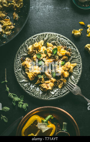 Leckere vegetarische Tortellini Pasta mit Gemüse und Pilzen auf Teller mit Gabel auf dunklen rustikalen Tisch Hintergrund, Ansicht von oben Stockfoto