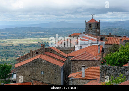 Blick über die Dächer zur Uhr oder zum Kirchturm mit silberfarbenem Hahnenfuß und die umliegende Landschaft in Monsanto, Portugal Stockfoto