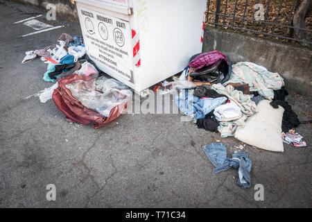 Alte Kleider und Müll um eine Sammelstelle (Müll/Recycling/Grobheit/bürgerlichen Sinn). Bergamo, Italien - 9. Januar 2019 Stockfoto