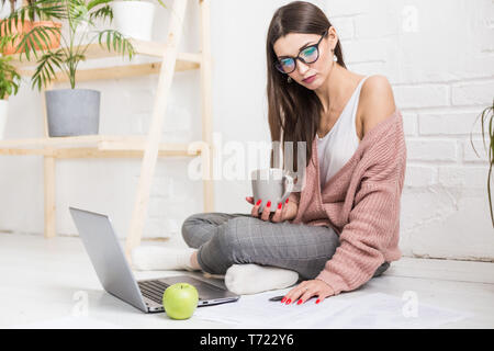 Junge Frau sitzt auf dem Boden in einem skandinavischen apartment Interieur mit einem Laptop, Studium der Rechtswissenschaften, freiberufliche Mädchen bei der Arbeit, Distance Learning student Stockfoto