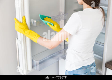Eine junge Frau von einem professionellen Reinigungsfirma reinigt bis zu Hause. Ein Mann wäscht die Küche der Kühlschrank in gelb Handschuhe mit Reinigung wäscht Stockfoto