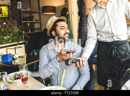 Junge attraktive hinduistischen Mann Bezahlen im Café mit berührungsloser smartphone Zahlung Stockfoto