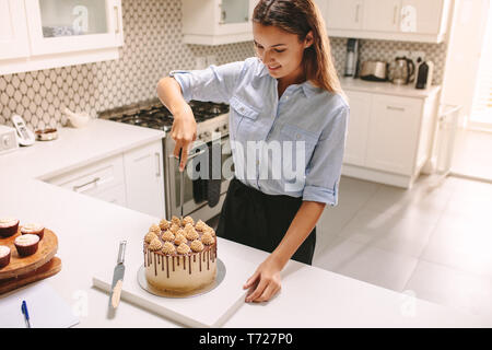 Köchin schneiden frisch zubereitete Kuchen in der Küche. Frau Konditor schneiden einen Kuchen. Stockfoto