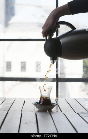 Weibliche hand gießt Kaffee ins Türkische Glas Stockfoto