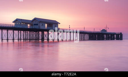 Penarth Pier, auf der South Wales Küste, in der Nähe von Cardiff, bei Sonnenaufgang. Der Himmel ist rot und orange, und das Meer ist glatt Stockfoto