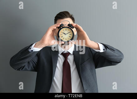 Man versteckt sich hinter Wecker auf grauem Hintergrund. Zeit-management Konzept Stockfoto