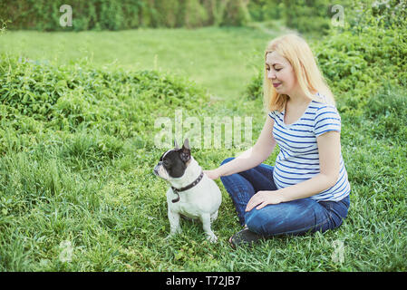 Schwangere Frau mit Hund im Grünen sonnige Natur. Gerne schwangere Frau mit ihr spielen pet im Park Stockfoto