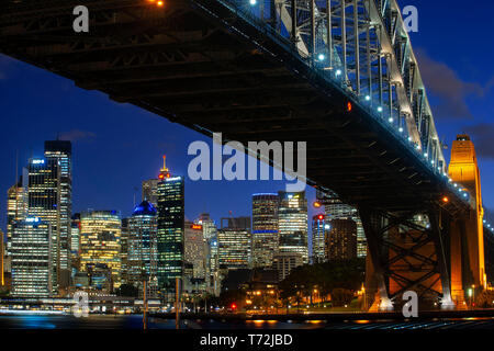 Seitliche Sicht auf die Sydney Harbour Bridge architektonische Sehenswürdigkeit und die Stadt bei Sonnenuntergang. Beleuchtete Bogen der Brücke in verschwommen Wasser Sydney, New widerspiegelt Stockfoto