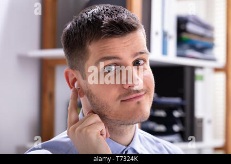 Glückliche junge Unternehmer trägt drahtlose Kopfhörer im Büro Stockfoto