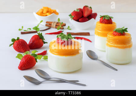 Traditionelle italienische süßes Dessert Panna cotta mit Mango Gelee mit Hauch von red hot chili Piri-Piri in Töpfen auf weissem Holztisch und embellis serviert. Stockfoto