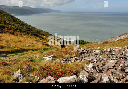 Wanderer absteigend der Felsen übersäte Tal von Bossington Hill gegen Porlock Bucht an der South West Coast Path von Minehead zu Porlock Wier mit v Stockfoto