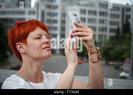 Nahaufnahme einer jungen Frau mit kurzen roten Haaren um die Stadt zu Fuß zu erkunden, die Bilder auf einem mobilen Smartphone, freier Platz für Text Stockfoto