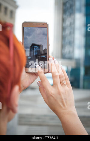 Nahaufnahme einer jungen Frau mit kurzen roten Haaren um die Stadt zu Fuß zu erkunden, die Bilder auf einem mobilen Smartphone, freier Platz für Text Stockfoto