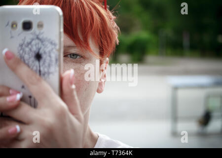 Nahaufnahme einer jungen Frau mit kurzen roten Haaren um die Stadt zu Fuß zu erkunden, die Bilder auf einem mobilen Smartphone, freier Platz für Text Stockfoto