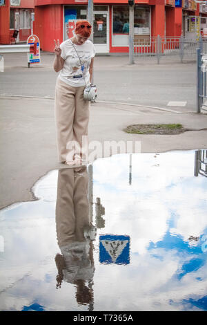 Nahaufnahme einer jungen Frau mit kurzen roten Haaren um die Stadt zu Fuß zu erkunden, Spiegel Reflexion in eine Pfütze auf dem Bürgersteig, freier Platz für Text Stockfoto