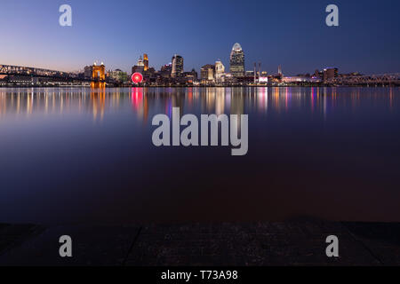 Die Sonne in einem klaren blauen Himmel über Cincinnati als die Lichter der Stadt von den Gebäuden und den Ohio River glättet an einem kühlen Frühling Abend entstehen. Stockfoto