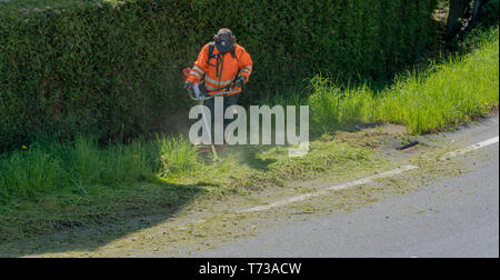 Ein stadtarbeiter Clearing am Straßenrand von Gras und Unkraut mit einem weed Eater Stockfoto
