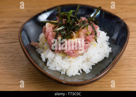 Schüssel mit Kobe Beef Tartare mit Eigelb, gehackte Zwiebel in ein Bett aus gedämpftem weißer Reis, serviert mit gebratenen Nori Algen, hölzernen Tisch Hintergrund Stockfoto