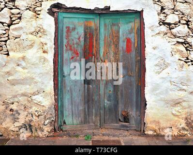 Eine sehr alte, marode und mit den unterschiedlichsten Farbablagerungen vorgesehen Holztür mit zwei Flügeltüren. Es gehört zu einer Hauswand eines baufälligen Abbr. Stockfoto