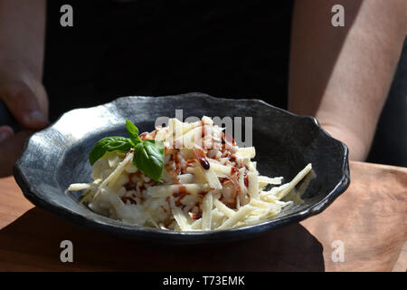Leckeres Risotto auf der schwarzen Keramik Platte gekrönt mit rasierten Käse Parmesan, Petersilie und Balsamico Essig unter der hellen Sonne durch Kellner ausgesetzt. Stockfoto