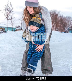 Happy girl Schwester spielt mit einem kleinen jungen Bruder. Im Winter draußen auf dem Hintergrund der Snow, Skate auf dem Eis. In Winterkleidung, Ruhe in die Neue Stockfoto