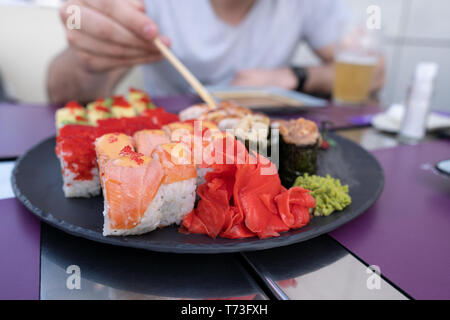 Sushi Nahaufnahme. Der Kerl isst Sushi und Brötchen mit Stäbchen. Stockfoto