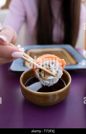 Weibliche hand Duns Sushi in Sojasauce. Das Mädchen isst Sushi und Brötchen mit Stäbchen. Stockfoto
