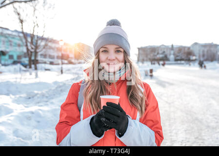 Nahaufnahme eines Mädchens im Winter draußen. In warme Kleidung, in die Hände der eine Tasse mit einem heißen Getränk aus Kaffee Tee. Gefühle der Freude, Spaß und Erholung im Freien Stockfoto