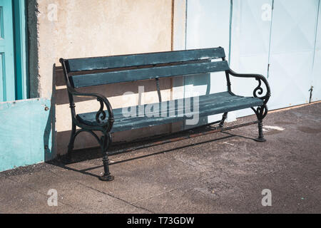 Ein bezauberndes Bild mit einer blauen Holzbank mit schmiedeeisernen Armlehnen, die eine einladende und malerische Sitzordnung schaffen. Stockfoto