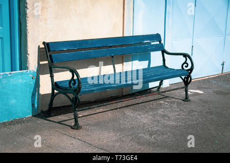 Ein bezauberndes Bild mit einer blauen Holzbank mit schmiedeeisernen Armlehnen, die eine einladende und malerische Sitzordnung schaffen. Stockfoto