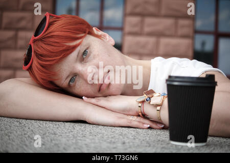 Nahaufnahme einer jungen Frau mit kurzen roten Haaren zu Fuß rund um die Stadt mit ein paar Tassen Kaffee, freier Platz für Text Stockfoto