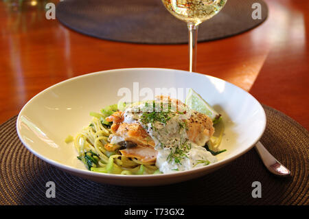 Frisch gebackenen Lachs auf Nudeln mit Spinat und Sellerie. Fischgericht serviert auf einem tiefen Teller mit einem Glas Weisswein. Das gesunde Essen. Stockfoto