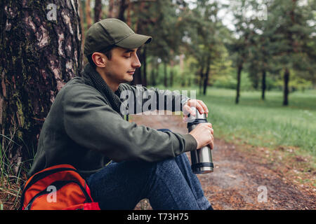 Man touristische öffnet Thermoskanne mit heißem Tee im Frühjahr Wald. Kerl in Ruhe. Camping, Reisen und Sport Konzept Stockfoto