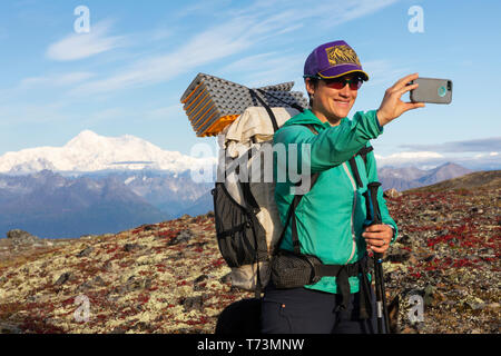 Frau beim Selfie beim Rucksackwandern mit Denali im Hintergrund, entlang des Kesugi Ridge Trail, Denali State Park an einem sonnigen Herbsttag, Southce... Stockfoto