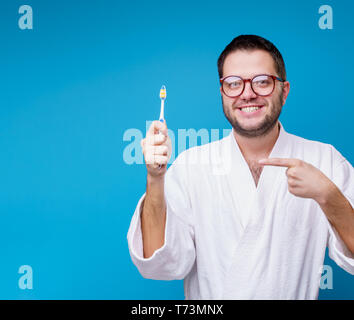 Foto von Mann mit Brille im weißen Mantel mit der Zahnbürste in der Hand auf leeren blauen Hintergrund Stockfoto