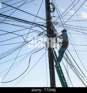 Elektriker Instandsetzung power line kabel auf eine Post, Französisch Hafen; Roatan, Bay Islands, Honduras Stockfoto