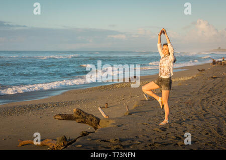 Chinesische Touristen am Strand von Hokitika eine Yoga Pose, Neuseeland Stockfoto