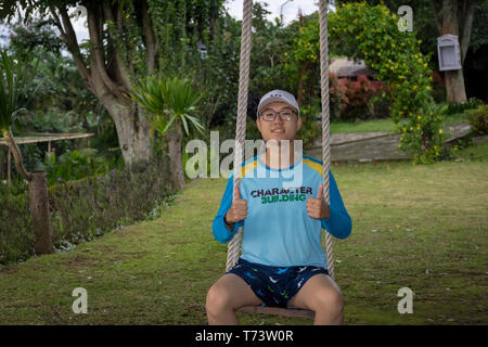 Ein glücklicher Mann sitzt auf einer Schaukel im Garten von Bandungan Hills Hotel und Resort in Semarang, Indonesien Stockfoto