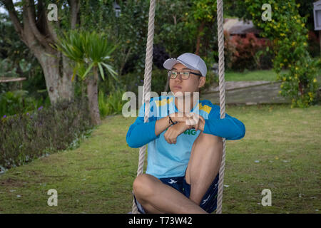 Ein glücklicher Mann sitzt auf einer Schaukel im Garten von Bandungan Hills Hotel und Resort in Semarang, Indonesien Stockfoto