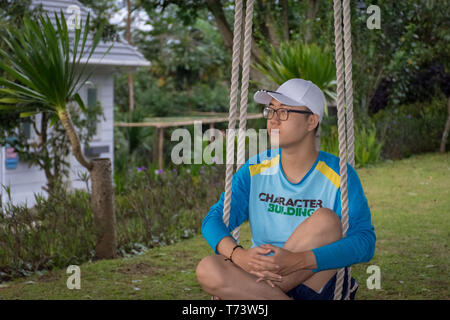 Ein glücklicher Mann sitzt auf einer Schaukel im Garten von Bandungan Hills Hotel und Resort in Semarang, Indonesien Stockfoto