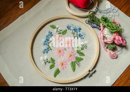 Bestickte Bouquet von wilden Blumen auf Baumwollstoff mit Holz- Bänder, farbigen Fäden, Schere und ein rotes Kissen für Nadeln abgedeckt Stockfoto