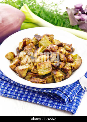 Auberginen gebraten mit Zwiebeln, Eiern und Gewürzen in einer Platte auf einem blau serviette, Basilikum, Lauch und Dill auf Holzbrett Hintergrund Stockfoto