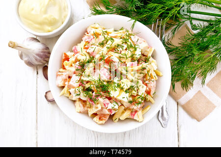 Salat von Crab Sticks, Käse, Knoblauch, Eier und Tomaten, gekleidet mit Mayonnaise in einer Platte, Küche Handtuch und Petersilie auf dem Hintergrund einer Licht werde Stockfoto