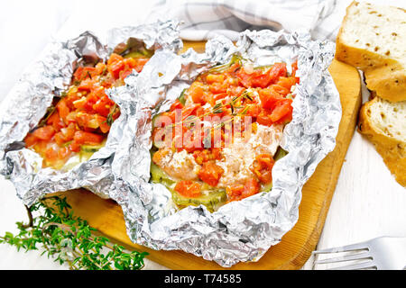 Rosa Lachs mit Zucchini, Tomaten, Zwiebeln, Knoblauch und Thymian, in Folie gebacken, Gabel und Brot auf ein weißes Holzbrett Hintergrund Stockfoto